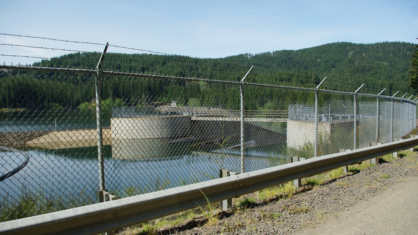 Hydropower facility perimeter fencing across natural terrain and water-control structures
