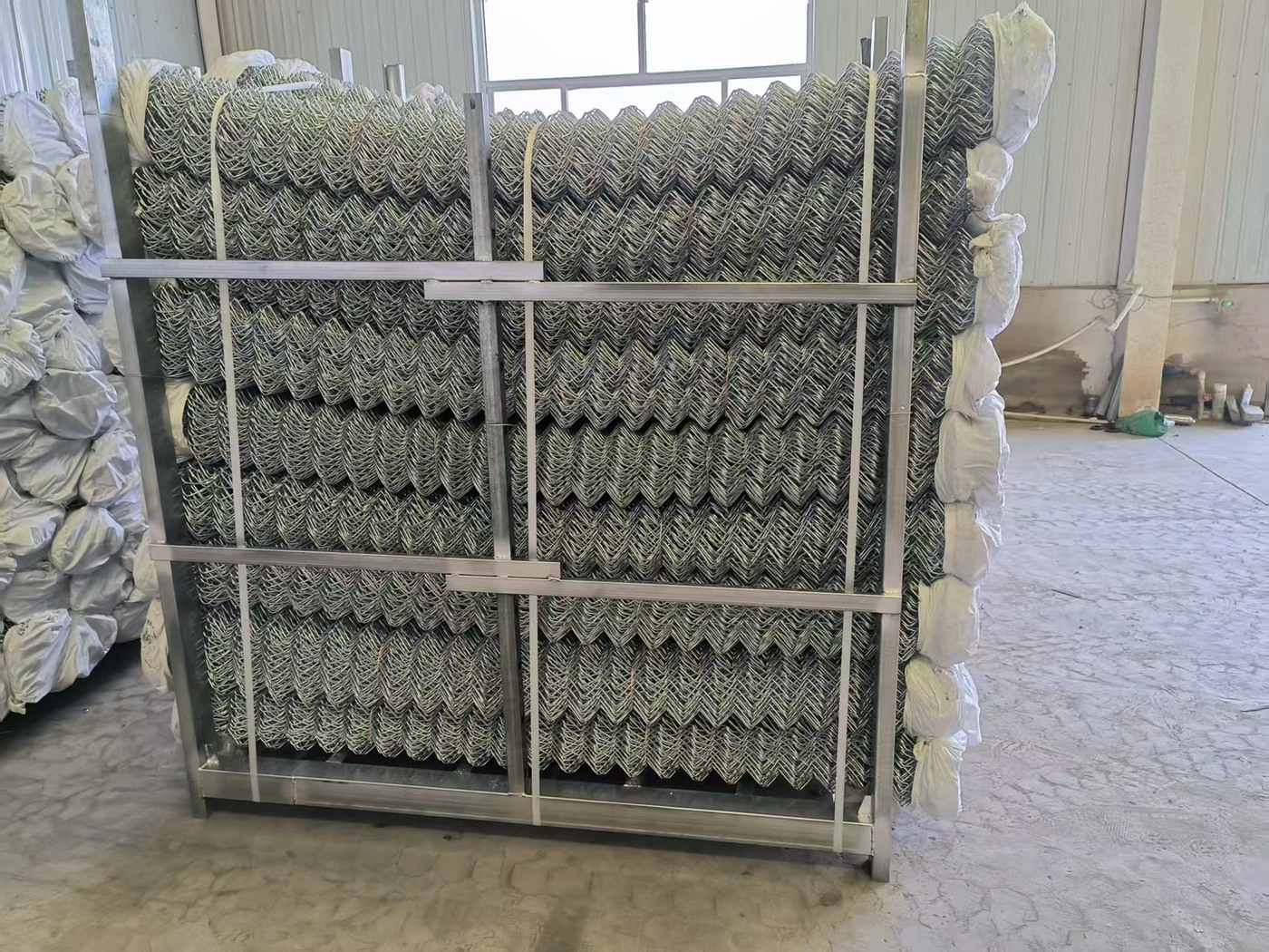 Stacked chain-link wire mesh rolls in a production facility
